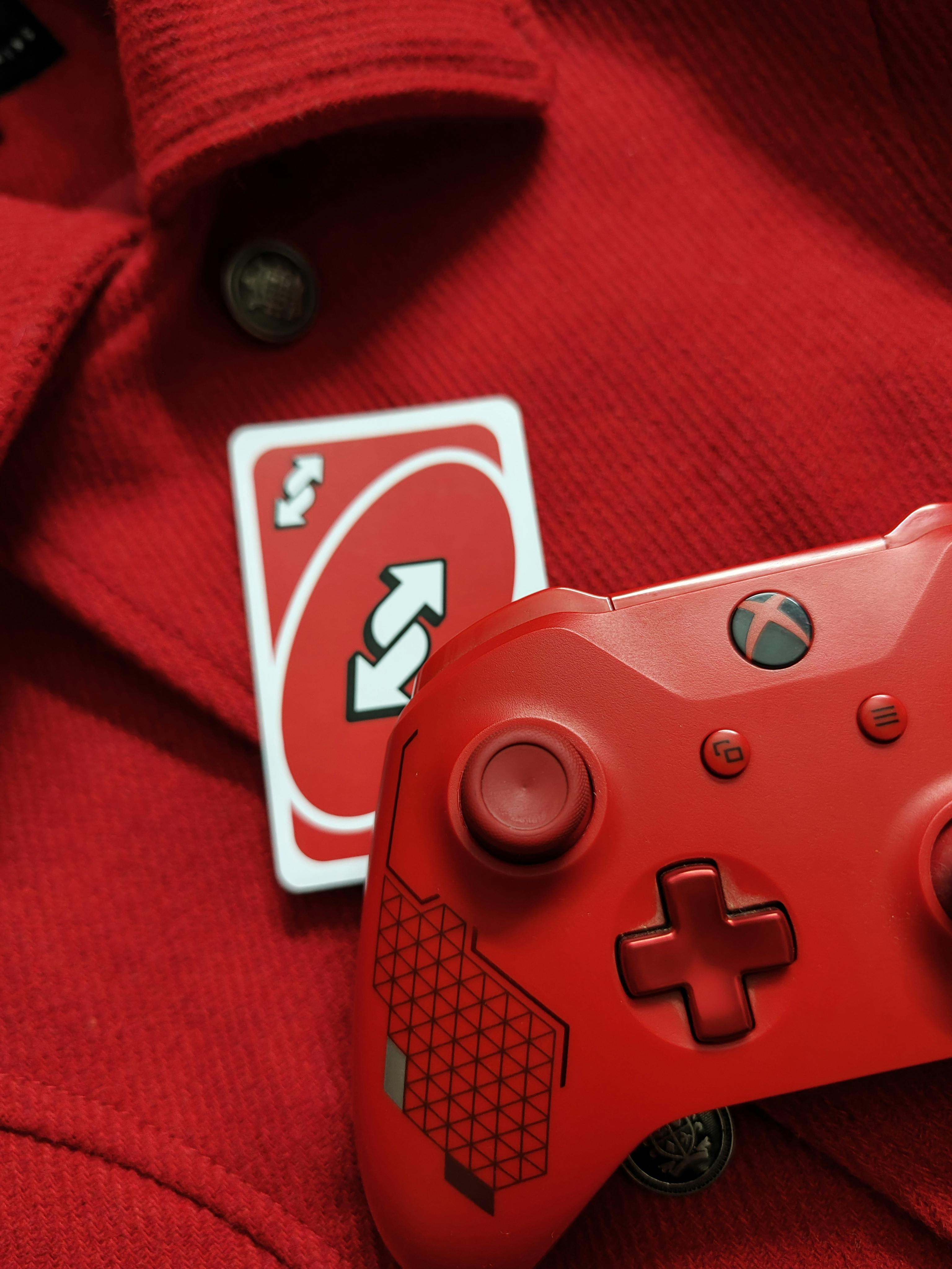 A red Xbox controller with a reverse Uno card on a red fabric background, perfect for gaming themes.